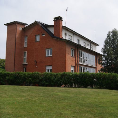 Vista de la finca con el cesped en primer plano y al fondo el edificio de la residencia